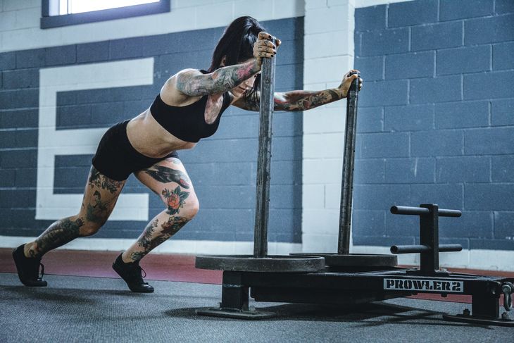 A woman pushing a sled in the gym. 